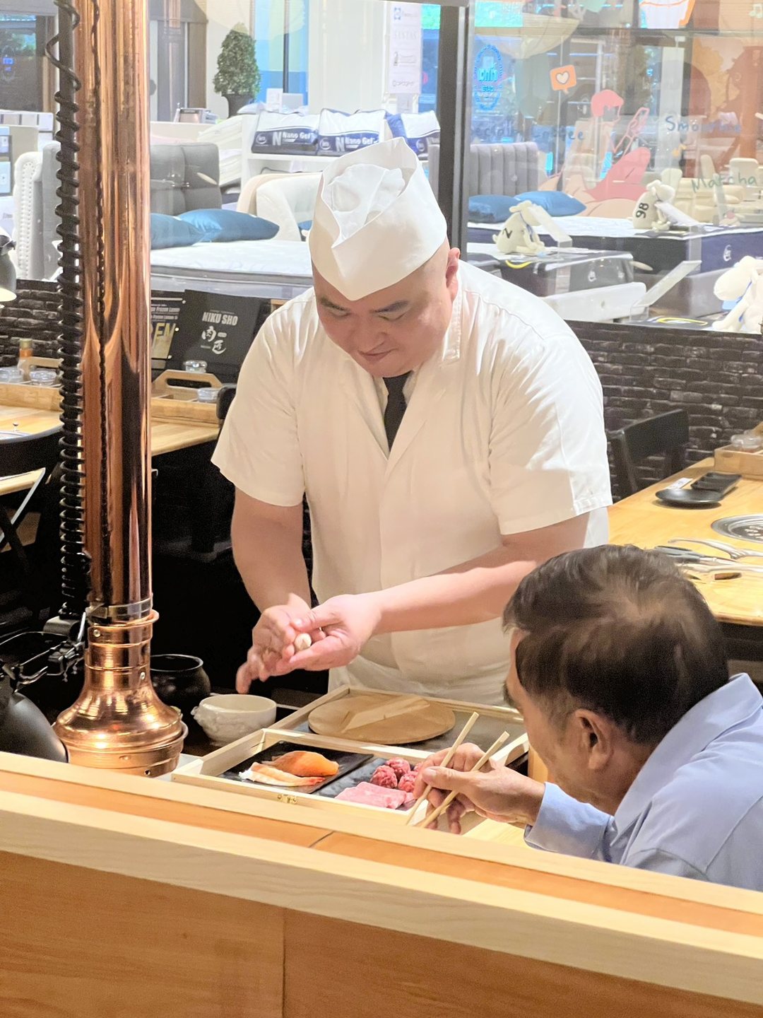 The chef presses a piece of sushi as a guest reaches in with chopsticks